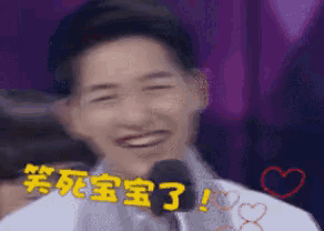 a man is laughing in front of a microphone with chinese writing on his face .