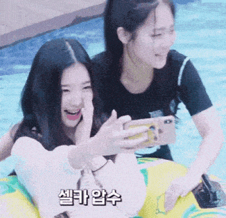 two girls are taking a selfie in a swimming pool while one is holding a cell phone .