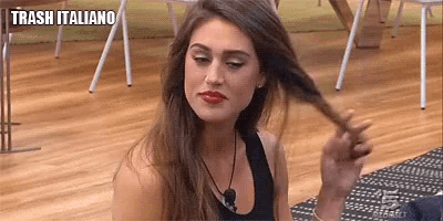a woman is sitting on the floor holding her hair in a room with a sign that says trash italiano .