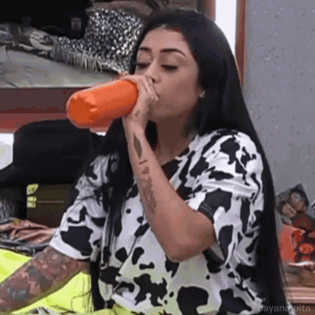 a woman in a cow print shirt is drinking from a bottle