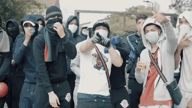 a group of people wearing face masks and hoodies are dancing .