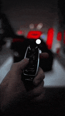 a person is holding a remote control in front of a black car