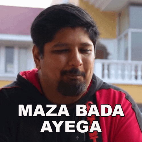 a man with a beard is wearing a red hoodie and says maza bada ayega