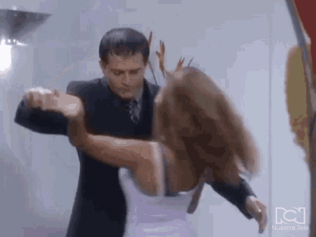 a man in a suit and tie is dancing with a woman in a white dress in front of a sign that says nuestra tele