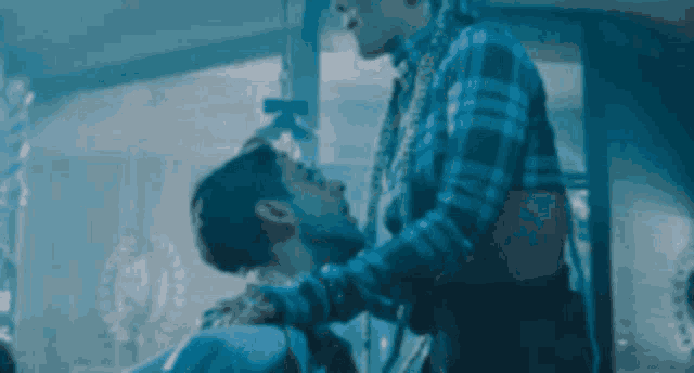 a man in a plaid shirt is holding another man 's head .