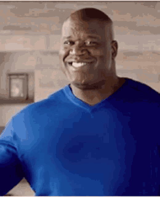 a man in a blue shirt is smiling while standing in a room .