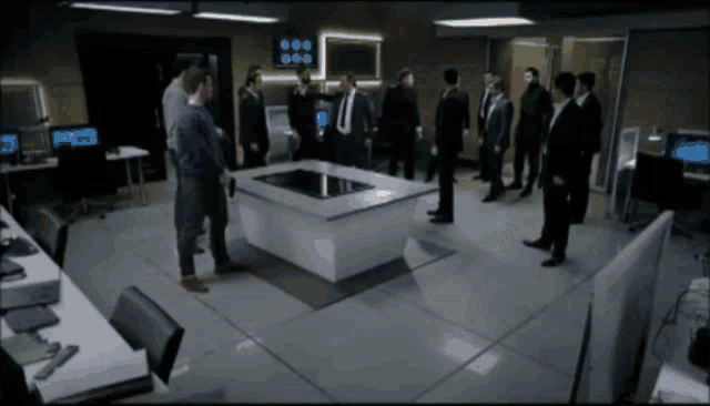a group of men are standing around a table with a monitor on it