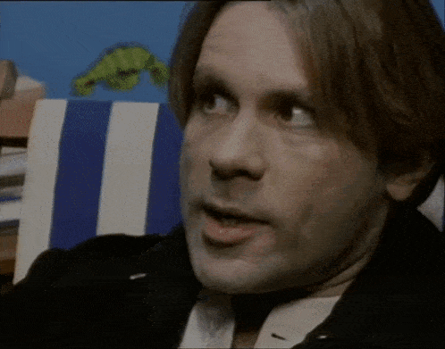 a close up of a man 's face with a blue and white striped chair in the background