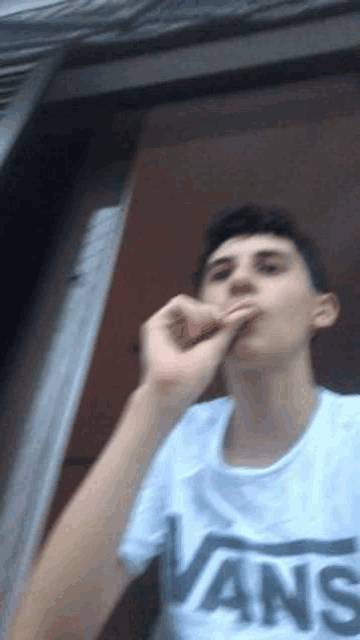 a young man wearing a white vans t-shirt smoking a cigarette