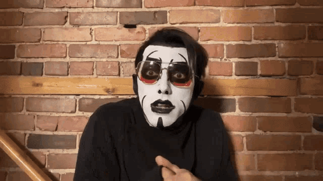 a man with a clown face painted on his face is pointing at something