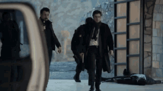 a man in a trench coat is walking past a dead man