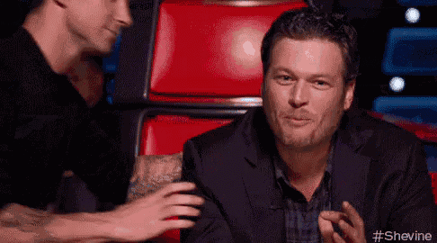 a man in a suit is sitting in a red chair talking to another man in a black shirt .
