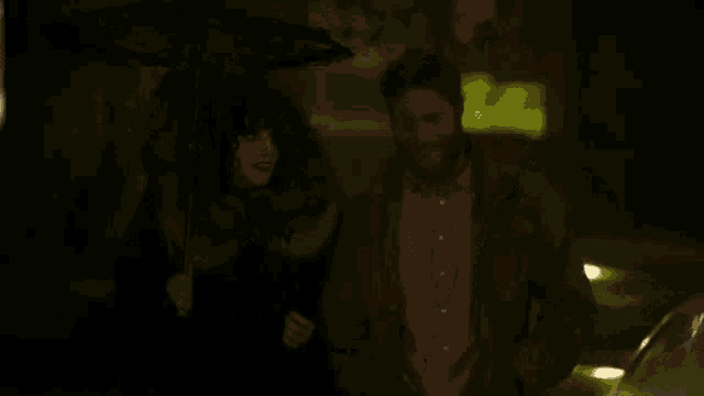 a man and a woman are walking down the street at night under an umbrella .