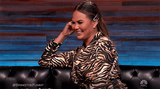 a woman wearing a zebra print shirt is sitting on a couch with a nbc logo on the bottom