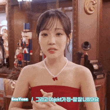 a woman wearing a red dress and a pearl necklace is standing in front of a nutcracker statue ..