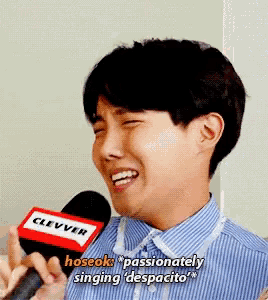 a young man is singing despacito into a microphone while wearing a blue and white striped shirt .