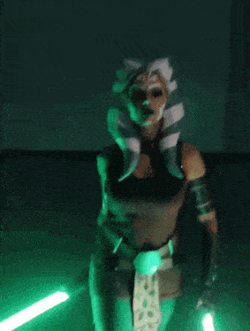 a woman in a star wars costume is holding a green lightsaber .