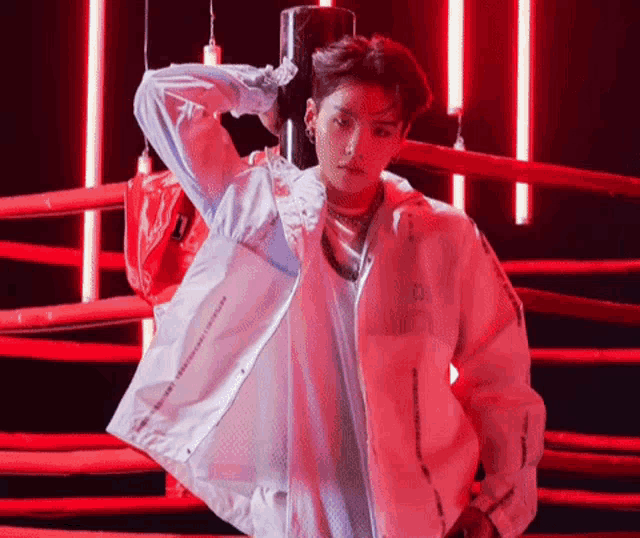 a man in a white jacket is standing in a boxing ring with red lights behind him