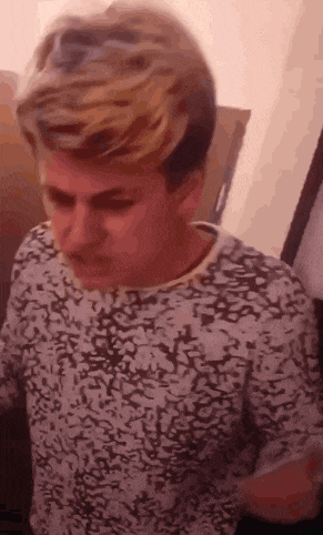 a man with blonde hair is wearing a white and black shirt .