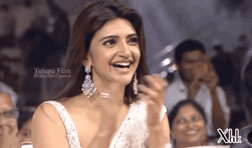 a woman in a white dress is smiling in front of a telugu film producer 's council logo