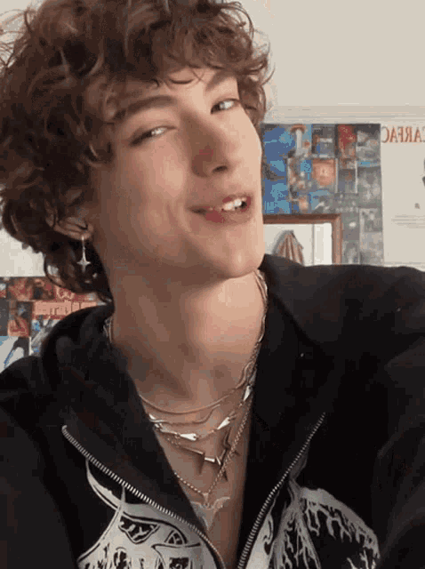 a young man with curly hair is wearing a black jacket and a skull necklace