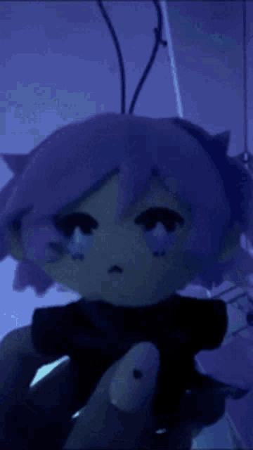 a person is holding a stuffed doll with purple hair and a sad face