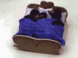 two stuffed penguins are sleeping in a bed with a blue blanket and pillows