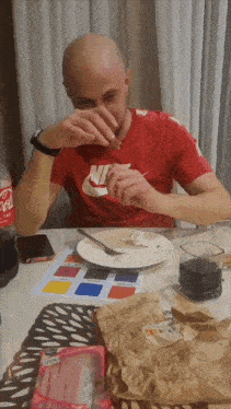 a man in a red nike shirt is sitting at a table eating food