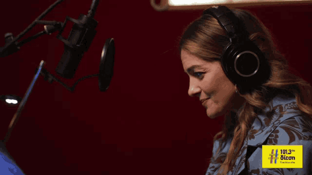 a woman is wearing headphones and smiling in front of a microphone that says 101.3 on it
