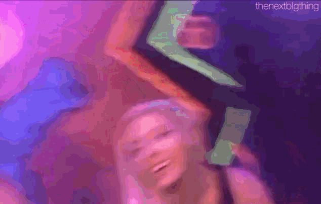 a woman is dancing in a dark room with a neon sign behind her .