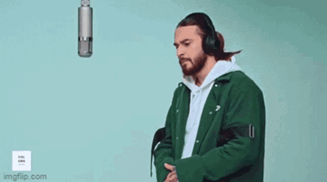 a man wearing headphones and a green jacket is singing into a microphone and the word nan is above him .
