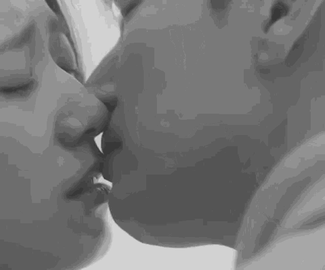 a black and white photo of a man and a woman kissing .