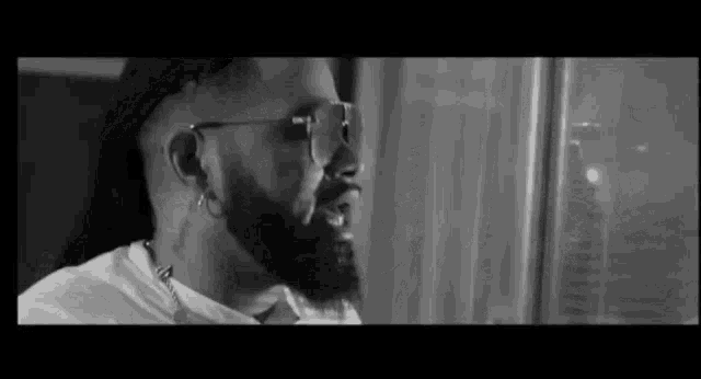 a black and white photo of a man with a beard and sunglasses looking out a window .
