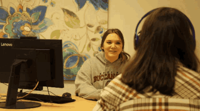a woman wearing a buccaneer sweatshirt sits in front of a lenovo monitor