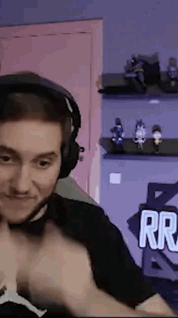 a man wearing headphones is sitting in front of a pink door and a shelf with figurines on it .