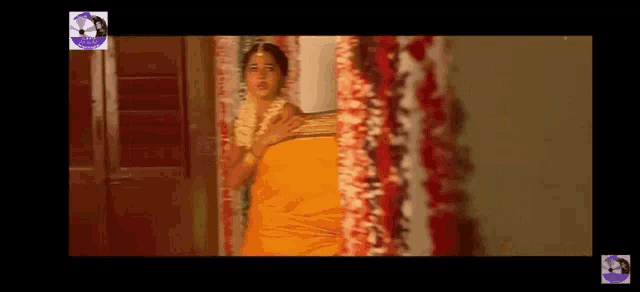 a woman in a yellow sari is standing in a room with flowers on the wall .