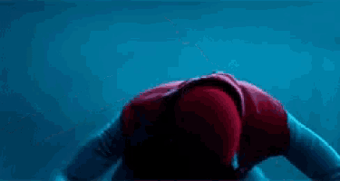 a man in a spiderman costume is kneeling down and pointing at something .