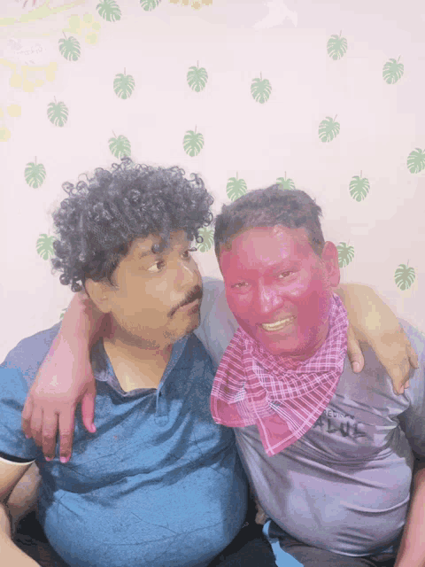 a man with red paint on his face is sitting next to another man with curly hair