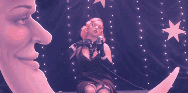 a woman sitting on a crescent moon with a microphone in her hand