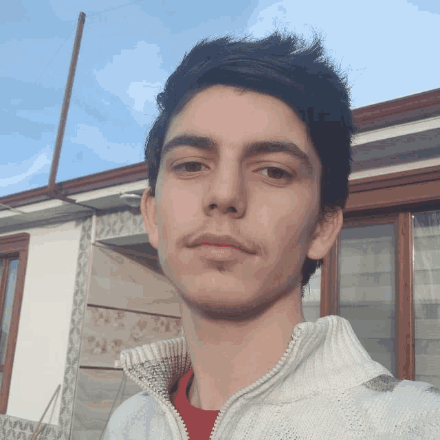 a young man wearing a white sweater and a red shirt poses for a picture
