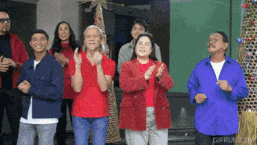 a group of people standing in front of a christmas tree and clapping