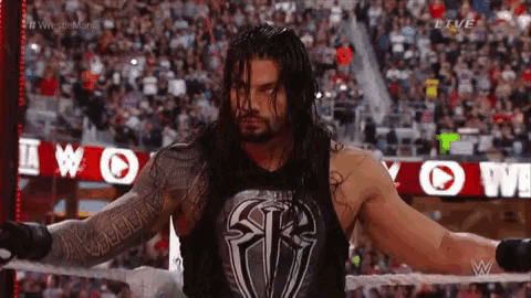 roman reigns is standing in a ring with his arms outstretched .
