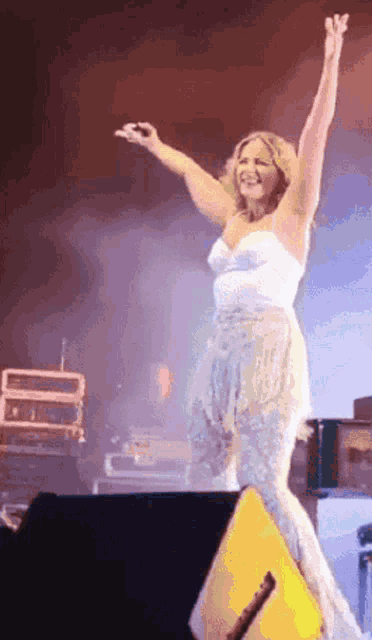 a woman in a white dress is standing on stage with her arms in the air