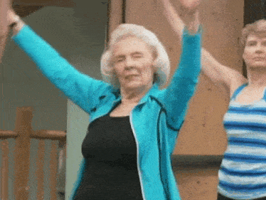 an elderly woman in a blue jacket is doing a yoga pose with her arms in the air .