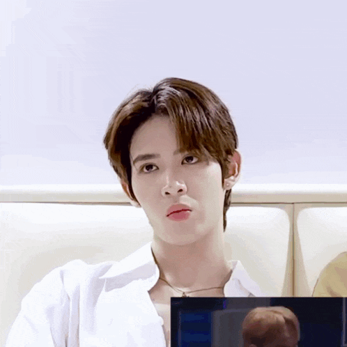 a young man in a white shirt is sitting on a couch looking at something