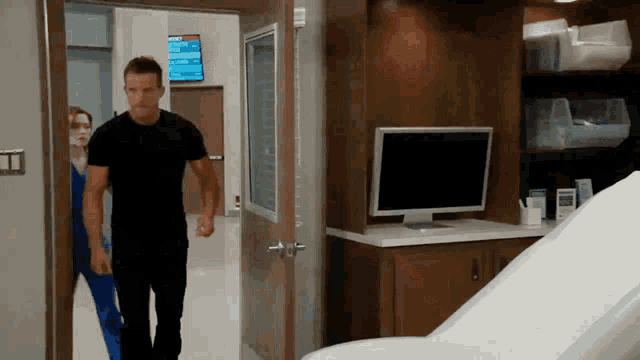 a man in a black shirt walks through a doorway in a hospital