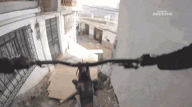 a person riding a bike down a narrow street with the words awesome on the bottom left