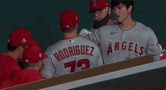 a group of baseball players are standing in the dugout talking to each other .