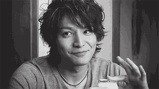 a man is sitting at a table holding a can of soda and smiling in a black and white photo .