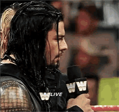 a man with long hair is holding a microphone that says w live